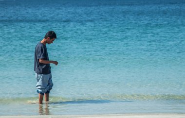 Genç adam sahilde geziniyor.