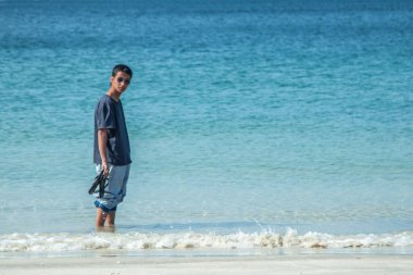 Genç adam sahilde geziniyor.