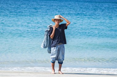 Şapkalı genç adam sahilde eğleniyor.