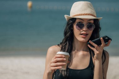 Kahve içen ve sesli mesaj gönderen genç bir kadın.