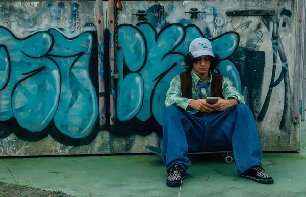 Kaykayın üzerinde oturan genç cep telefonu kullanıyor.