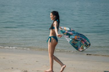 Eşarplı güzel bir kadın kumsalda yürürken rüzgarda sallanıyor.