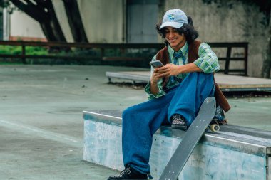 Parktaki bankta cep telefonu kullanan genç bir çocuk.