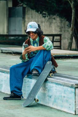 Genç bir çocuk parktaki bankta cep telefonuyla konuşuyor.