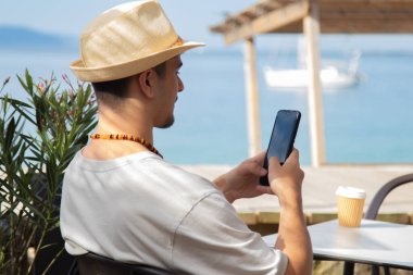 Plaj barında cep telefonu kullanan genç bir adam.