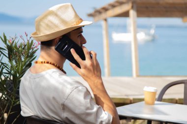 Plaj barında cep telefonu kullanan genç bir adam.