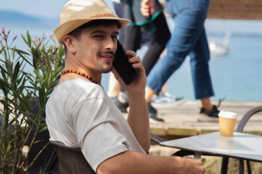 Plaj barında cep telefonuyla konuşan rahat genç bir adam.