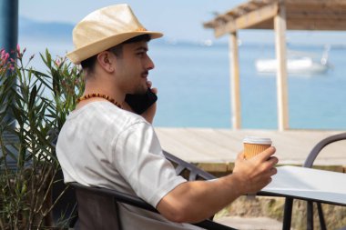 Cep telefonlu rahat genç adam plaj barında kahve içiyor.