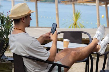 Plaj barında cep telefonu kullanan genç bir adam.