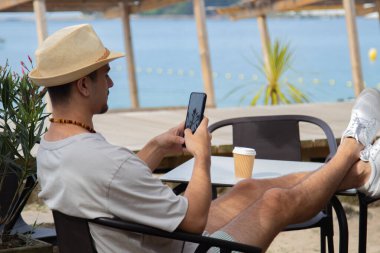 Plaj barında cep telefonu kullanan genç bir adam.