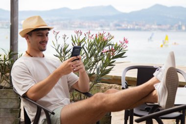 Plaj barında cep telefonu kullanan genç bir adam.