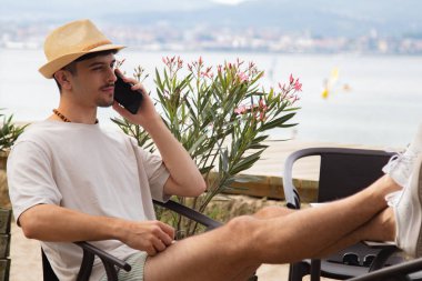 Plaj barında cep telefonuyla konuşan rahat genç bir adam.