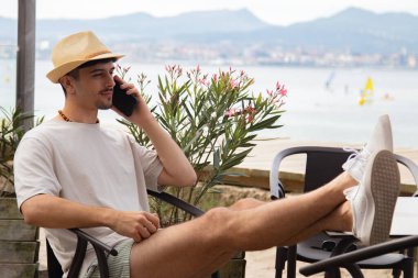 Plaj barında cep telefonuyla konuşan rahat genç bir adam.