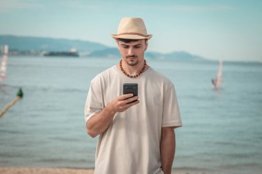 Elinde cep telefonu tutan yakışıklı bir adam ve tropikal arka planda mesaj atıyor.