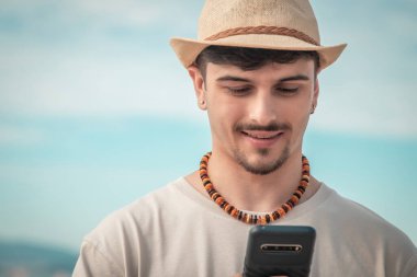 Elinde cep telefonu tutan yakışıklı bir adam ve tropikal arka planda mesaj atıyor.