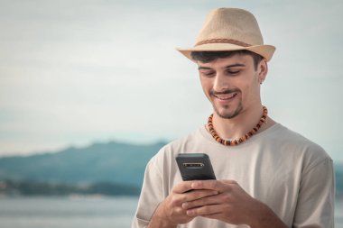 Elinde cep telefonu tutan yakışıklı bir adam ve tropikal arka planda mesaj atıyor.