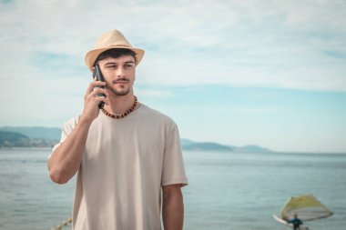 Genç adam sahilde akıllı telefon kullanıyor.