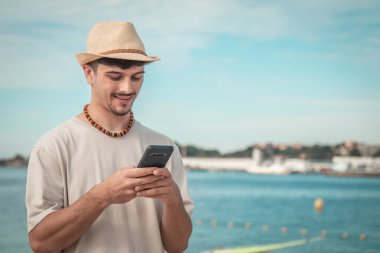 Elinde cep telefonu tutan yakışıklı bir adam ve tropikal arka planda mesaj atıyor.