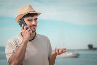 Genç adam sahilde cep telefonuyla konuşuyor.