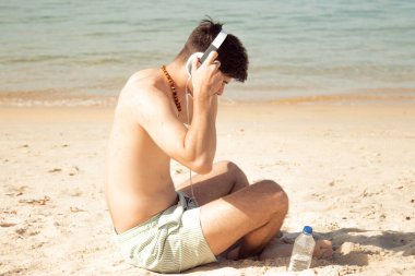 Plajda kulaklığı ve su şişesi olan rahat bir adam.