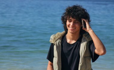 Sahilde cep telefonuyla gülümseyen genç adam.