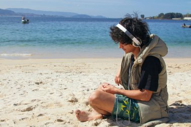 Genç adam plajda kulaklık takıyor.