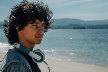 Kulaklıklı genç adam denizin önünde gülümsüyor.