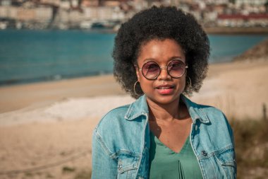 Güneş gözlüklü, plaj geçmişi olan Afro-Amerikan kadın portresi.