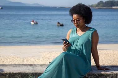 Plaj geçmişi olan genç bir kadın telefonundan mesajlarını okuyor.