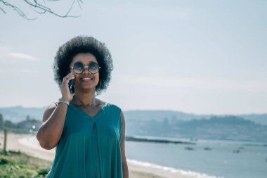 Gülümseyen genç Afrikalı kadın cep telefonu kullanıyor.