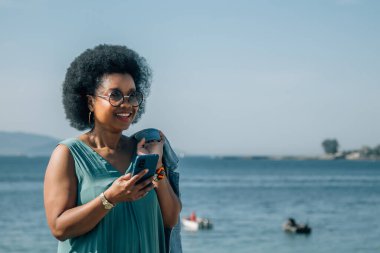 Plaj geçmişinde akıllı telefonu olan Afrikalı Amerikalı bir kadın.