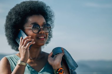 Plaj geçmişinde akıllı telefonu olan Afrikalı Amerikalı bir kadın.