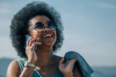 Plaj geçmişinde akıllı telefonu olan Afrikalı Amerikalı bir kadın.