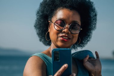 Genç bir kadın özçekim yapıyor ya da sahilin arka planında akıllı telefonlu canlı bir video çekiyor.