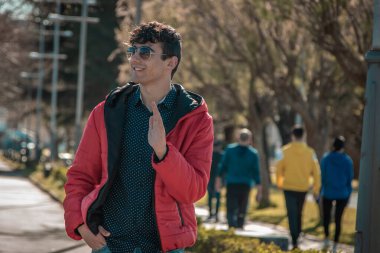 Güneş gözlüklü yakışıklı genç adam sokakta el sallıyor.