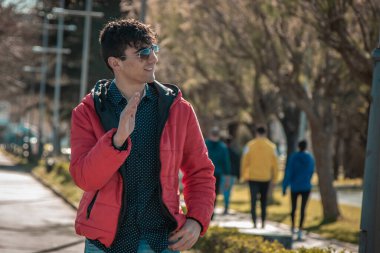 Güneş gözlüklü yakışıklı genç adam sokakta el sallıyor.