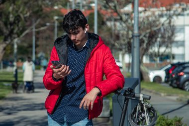 Sokakta müzik dinlerken elektrikli scooterına yaslanan genç bir şehirli.