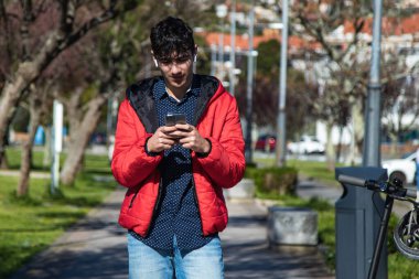 Kulaklıklı genç adam parkta akıllı telefonunu izliyor.