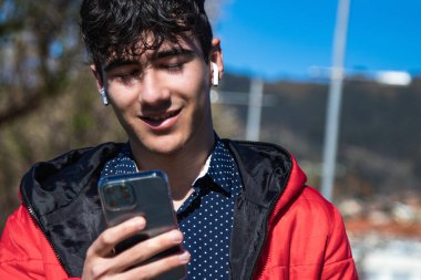 Kulaklıklı genç adam parkta akıllı telefonunu izliyor.