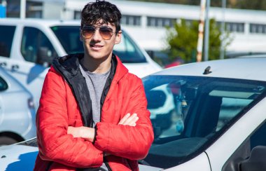 Sokakta kollarını kavuşturmuş güneş gözlüklü yakışıklı bir genç.