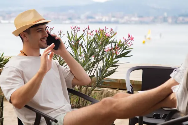 Plaj barında cep telefonuyla konuşan ve el sallayan rahat genç adam.