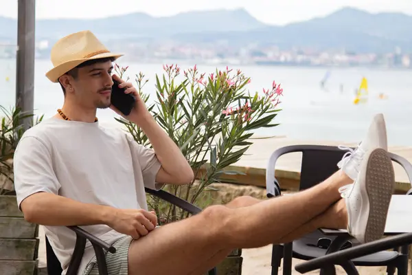 Plaj barında cep telefonuyla konuşan rahat genç bir adam.