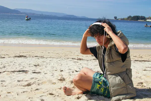 Genç adam plajda kulaklık takıyor.