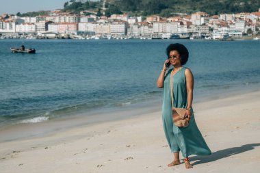 Sahilde akıllı telefonuyla konuşan Afrikalı Amerikalı kadın.