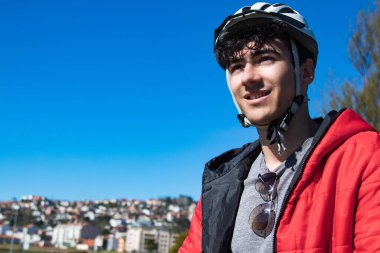 Sokakta elektrikli scooter kullanan kasklı genç bir adam.