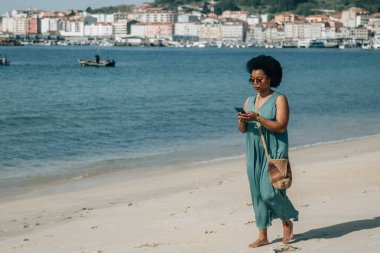 Sahildeki Afrikalı kadın akıllı telefondan mesaj okuyor., 