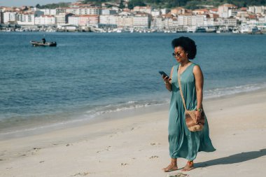 Sahildeki Afrikalı kadın akıllı telefondan mesaj okuyor., 