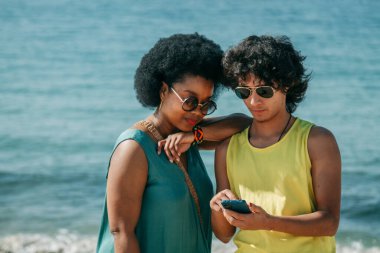 Sahilde akıllı telefona bakan çok ırklı bir çift.