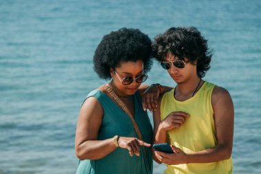 Sahilde akıllı telefona bakan çok ırklı bir çift.