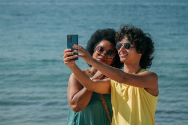 Çok ırklı bir çift selfie çekiyor ya da sahilde akıllı telefonlu canlı bir video çekiyor.